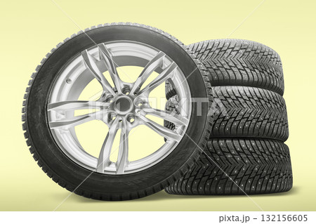 A new set of four studded winter tires sits beside a stylish alloy rim, prepared for replacement at a tire shop. Perfect for winter driving conditions. 132156605