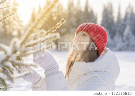 Woman inspecting snow-covered pine tree in winter landscape during sunny afternoon 132156610