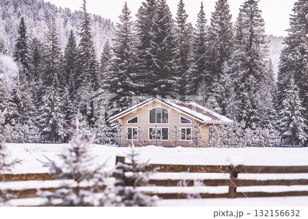 Charming cabin rests peacefully in a snowy landscape, surrounded by tall, snow-covered pine trees. Tranquil setting captures the beauty of winter in the mountains, with a wooden fence framing scene. Charming cabin rests peacefully in a snowy landscape, surrounded by tall, snow-covered pine trees. Tranquil setting captures the beauty of winter in the mountains, with a wooden fence framing scene. 132156632