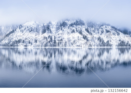 A tranquil winter landscape with snowcovered mountains and serene water reflections A tranquil winter landscape with snowcovered mountains and serene water reflections 132156642