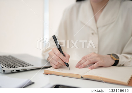 Office worker or clerk holding a fountain pen writing in notebook while sitting at table in office. Office worker or clerk holding a fountain pen writing in notebook while sitting at table in office. 132156656