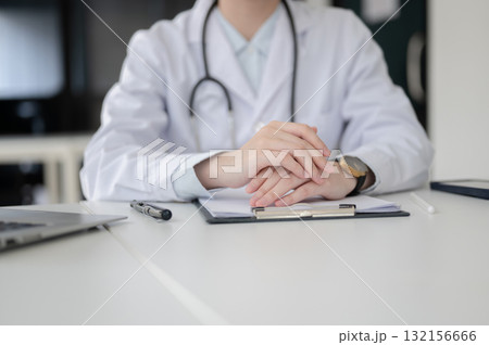 Doctor with stethoscope clasping hands on clipboard with document sitting at table in diagnosis room 132156666