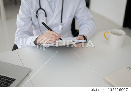 Top view of female doctor with stethoscope writing with pen on clipboard at table in diagnosis room Top view of female doctor with stethoscope writing with pen on clipboard at table in diagnosis room 132156667