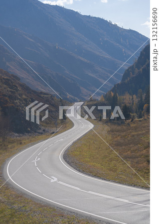 A winding road stretches through majestic mountains under a clear sky. This scenic route beckons travelers to explore the beautiful landscape and enjoy nature's tranquility. A winding road stretches through majestic mountains under a clear sky. This scenic route beckons travelers to explore the beautiful landscape and enjoy nature's tranquility. 132156690