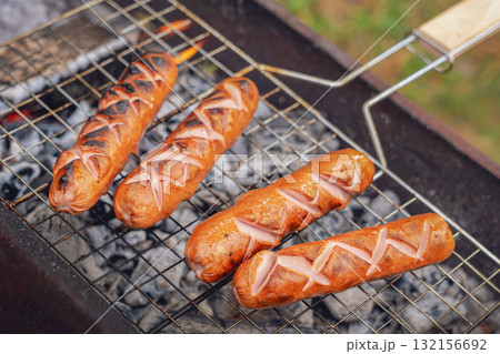 Juicy grilled sausages sizzling on a backyard grill during an autumn picnic in nature close up 132156692