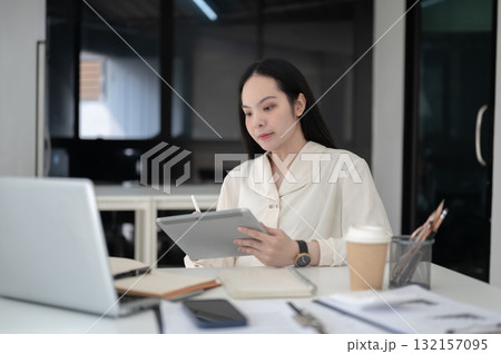 Businesswoman or office worker is holding a stylus pen writing on tablet sitting at table in office. 132157095