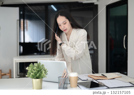 Businesswoman or female office worker is talking on the smartphone while leaning over working table. Businesswoman or female office worker is talking on the smartphone while leaning over working table. 132157105