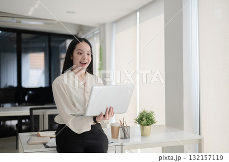 Female office worker looking surprised as she look at laptop and standing in front of working table. 132157119