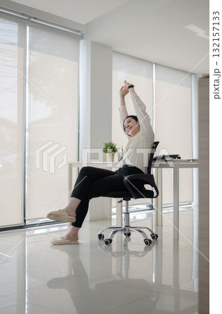 Female office worker or businesswoman sitting with both arm raised on swivel chair in empty office. Female office worker or businesswoman sitting with both arm raised on swivel chair in empty office. 132157133