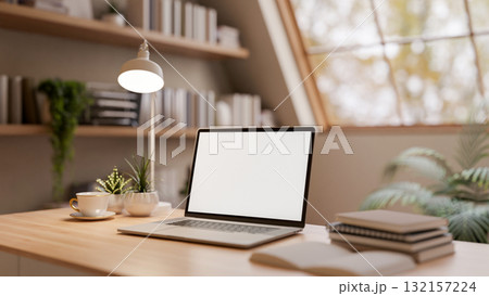 White screen laptop with coffee cup and books on wooden table in the bright room under roof window White screen laptop with coffee cup and books on wooden table in the bright room under roof window 132157224