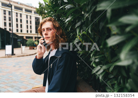 Young man talking on the phone in an urban setting surrounded by greenery 132158354