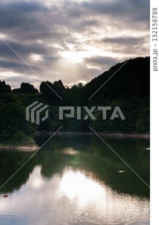 中秋の奈良布目ダム　雲間から覗く夕日によって明るく照らされる湖面① 132158789