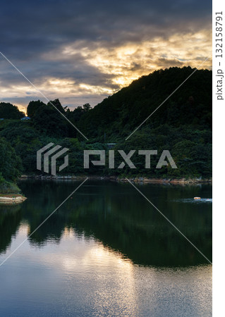 中秋の奈良布目ダム　山際で黄金色に染まる雲を映す湖面 132158791