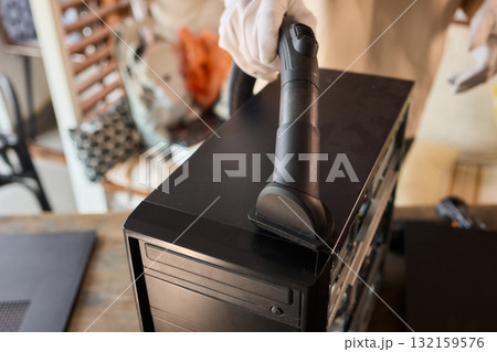 A man cleans a computer case with a vacuum in a bright room, stressing workspace tidiness A man cleans a computer case with a vacuum in a bright room, stressing workspace tidiness 132159576