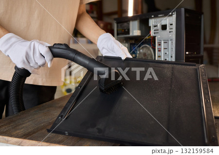 A man cleans a computer case with a vacuum in a bright room, stressing workspace tidiness 132159584