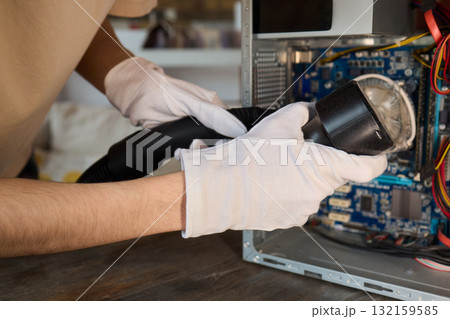 A man cleans a computer case with a vacuum in a bright room, stressing workspace tidiness A man cleans a computer case with a vacuum in a bright room, stressing workspace tidiness 132159585