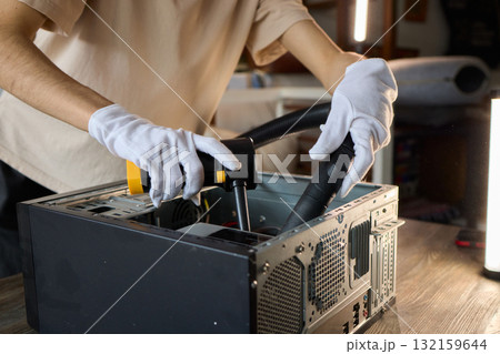 A man cleans a computer case with a vacuum in a bright room, stressing workspace tidiness A man cleans a computer case with a vacuum in a bright room, stressing workspace tidiness 132159644