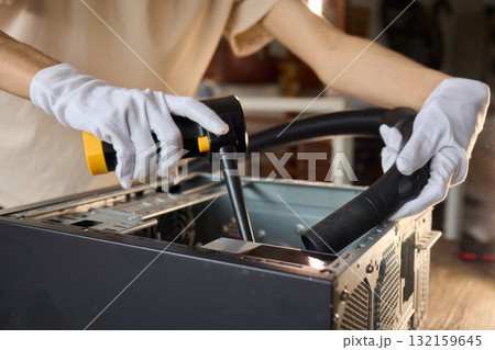A man cleans a computer case with a vacuum in a bright room, stressing workspace tidiness A man cleans a computer case with a vacuum in a bright room, stressing workspace tidiness 132159645