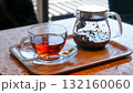 木製トレイに置かれたガラスのカップに注がれた紅茶と茶葉の入ったティーポット 132160060