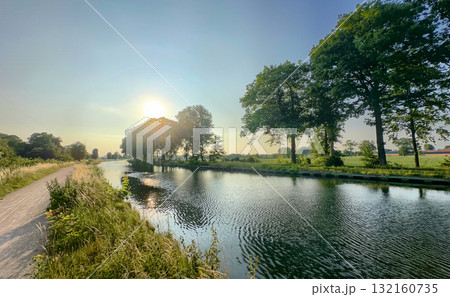 A calm river flows gently, with majestic trees reflecting the vibrant sunset colors 132160735