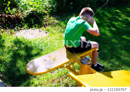 Young boy exercising outdoors on yellow fitness equipment. Young boy exercising outdoors on yellow fitness equipment. 132160767