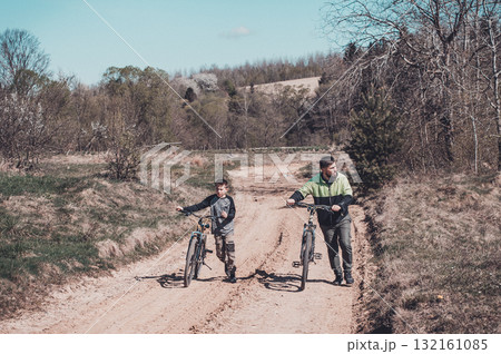 Father and son walking bikes on a country road, enjoying a sunny day outdoors. Father and son walking bikes on a country road, enjoying a sunny day outdoors. 132161085