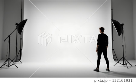 An individual standing between two rows of photography equipment set against a plain background 132161931