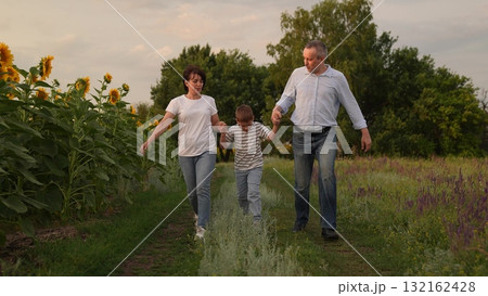 Happy family running together in nature, Joyful parents and child in the countryside, Family bonding in a sunflower field, Carefree moments with mom, dad, and kid, Parents and child enjoying outdoor 132162428