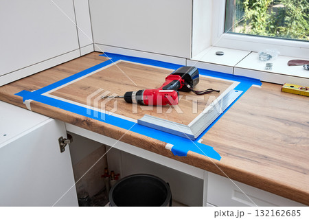 red cordless electric drill screwdriver and measuring tape on kitchen countertop. Kitchen cabinet installation 132162685