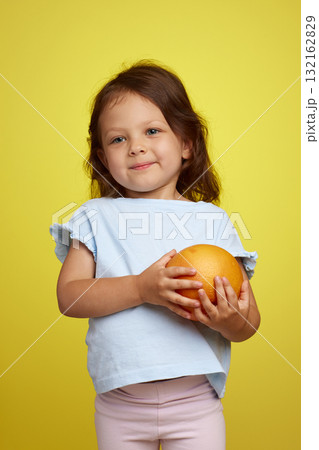 cute Caucasian little child girl holding grapefruit on yellow background 132162829