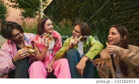 Four friends laughing and sharing burgers and fries in urban park 132162913