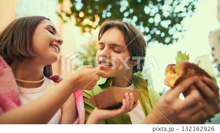 Young woman feeding fry to cheerful man smiling together outdoors Young woman feeding fry to cheerful man smiling together outdoors 132162926