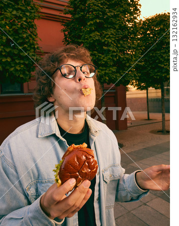 Cheerful young man eating burger on city street enjoying carefree moment Cheerful young man eating burger on city street enjoying carefree moment 132162934