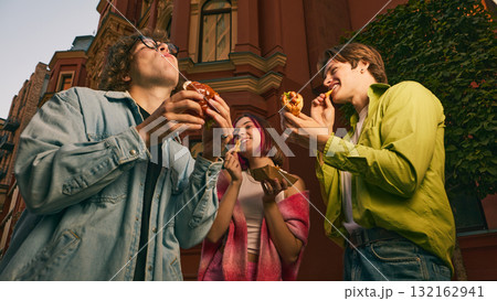 Group of young friends eating burgers and fries together on city street Group of young friends eating burgers and fries together on city street 132162941