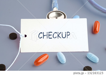 A health checkup reminder card sits among various pills, emphasizing the need for regular medical assessments to ensure overall well-being and early disease detection 132163123