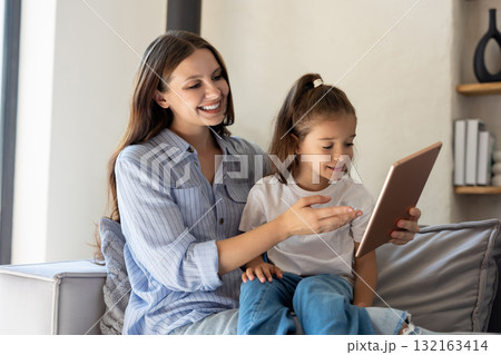Mom and child sitting on couch holding digital tablet 132163414