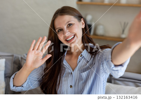Smiling female taking selfie and showing greeting gesture waving hand Smiling female taking selfie and showing greeting gesture waving hand 132163416