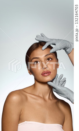 Woman face examined by doctor hands in gloves showing precision calmness and professional confidence Woman face examined by doctor hands in gloves showing precision calmness and professional confidence 132164703