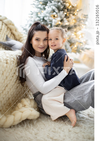 A mother and her young daughter share a tender moment, embracing each other with a Christmas tree in the background. A mother and her young daughter share a tender moment, embracing each other with a Christmas tree in the background. 132165016