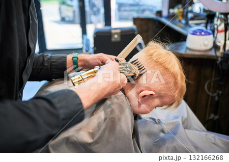 Little boy getting his first haircut. Back view of hairdresser shaving head. Cute client in barbershop. Little boy getting his first haircut. Back view of hairdresser shaving head. Cute client in barbershop. 132166268