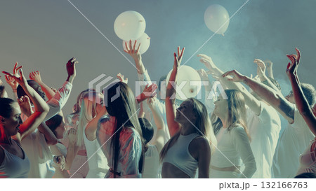Excited crowd in white dancing with balloons under soft stage lights Excited crowd in white dancing with balloons under soft stage lights 132166763