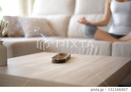 Incense stick burning in foreground and woman doing yoga 132166807