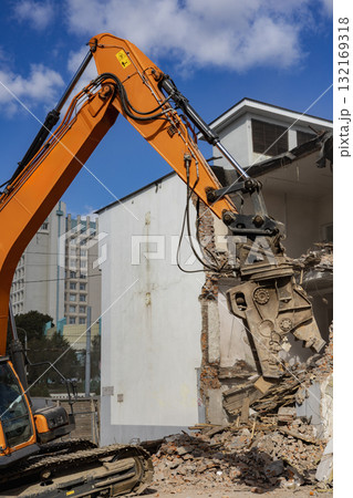 Demolition of a building using heavy machinery in an urban environment on a sunny day Demolition of a building using heavy machinery in an urban environment on a sunny day 132169318