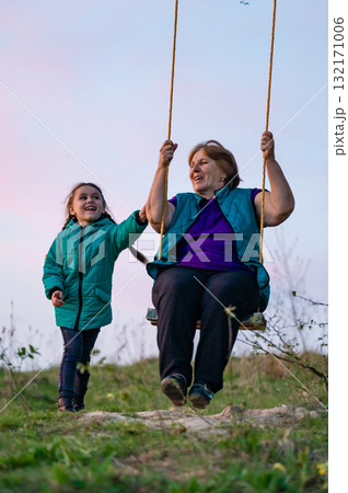 Grandmother and granddaughter sharing a joyful swing ride at sunset. Precious moment of intergenerational connection and playful fun. 132171006