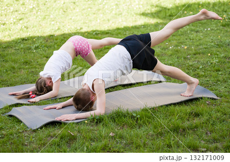 Kids doing yoga outdoors on mats. Healthy lifestyle and flexibility exercises. 132171009
