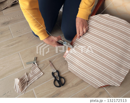 Anonymous person restore old vintage chair in home. Fabric replacement. Antique furniture and modern striped linen and cotton fabric. Hobbies, crafts, and retro-minimalist style. 132172513