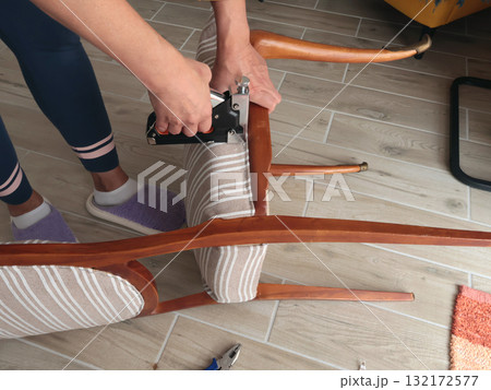 Anonymous person restore old vintage chair in home. Fabric replacement. Antique furniture and modern striped linen and cotton fabric. Hobbies, crafts, and retro-minimalist style. 132172577