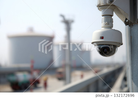A CCTV camera is mounted high on a building in an industrial plant or factory. A CCTV camera is mounted high on a building in an industrial plant or factory. 132172696