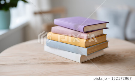 Stack of pastel hardcover books on wooden table in bright cozy home interior 132172967