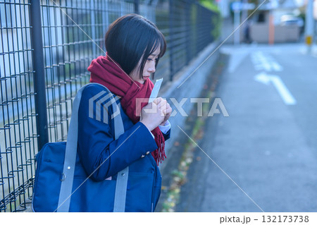 寒い日に部活で登下校する女子高生　冬服でカイロを持ち友達を待つ高校生　登校下校　 132173738